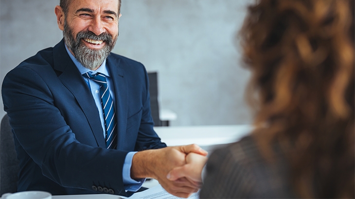 A smiling businessman shaking hands with a businesswoman.